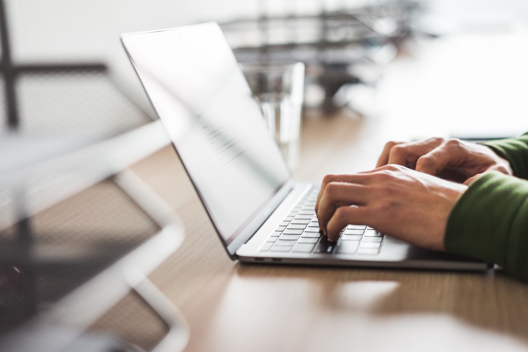 Person tippt auf einer Laptop-Tastatur an einem Tisch in einem hellen Raum