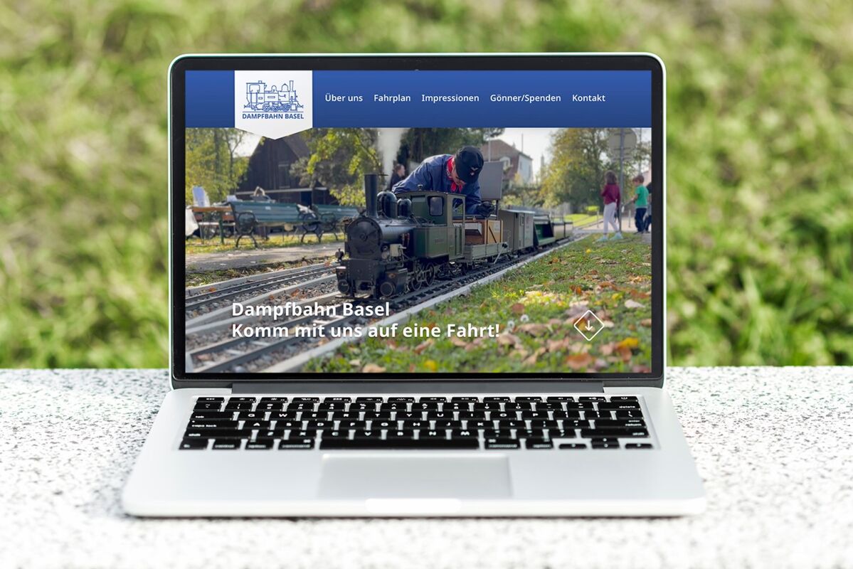 Offener Laptop zeigt eine Website mit einer kleinen Dampflok und dem Text "Dampfbahn Basel Komm mit uns auf eine Fahrt"