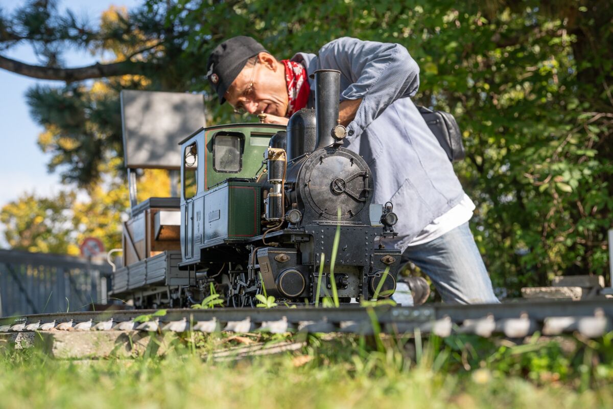 Eine Person arbeitet im Freien an einer kleinen Dampflokomotive auf Gleisen