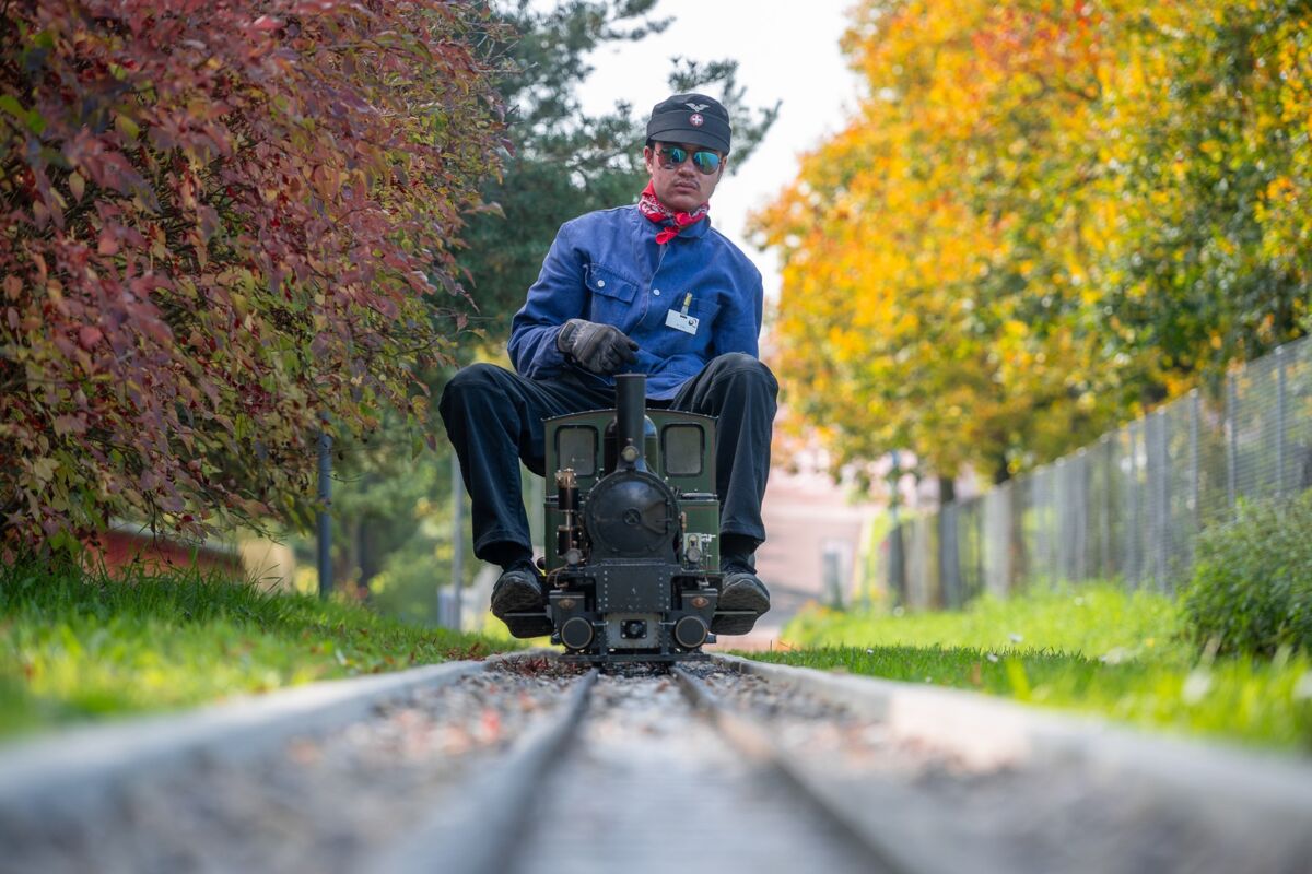 Eine Person fährt auf einer kleinen Lokomotive auf schmalen Gleisen zwischen Hecken und Bäumen